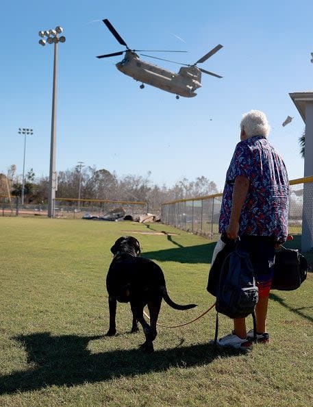 Tom O'Sullivan and his dog Jack look on as a Florida National Guard chinook lands as they prepare to be evacuated on October 2, 2022, in Pine Island, Florida. Residents are being encouraged to leave because the only road onto the island is impassable and electricity and water remain knocked out after Hurricane Ian passed through the area.