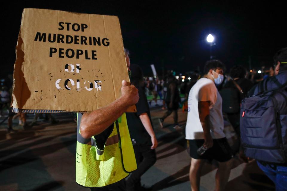 A protester holds a placard reading: Stop murdering people of color.