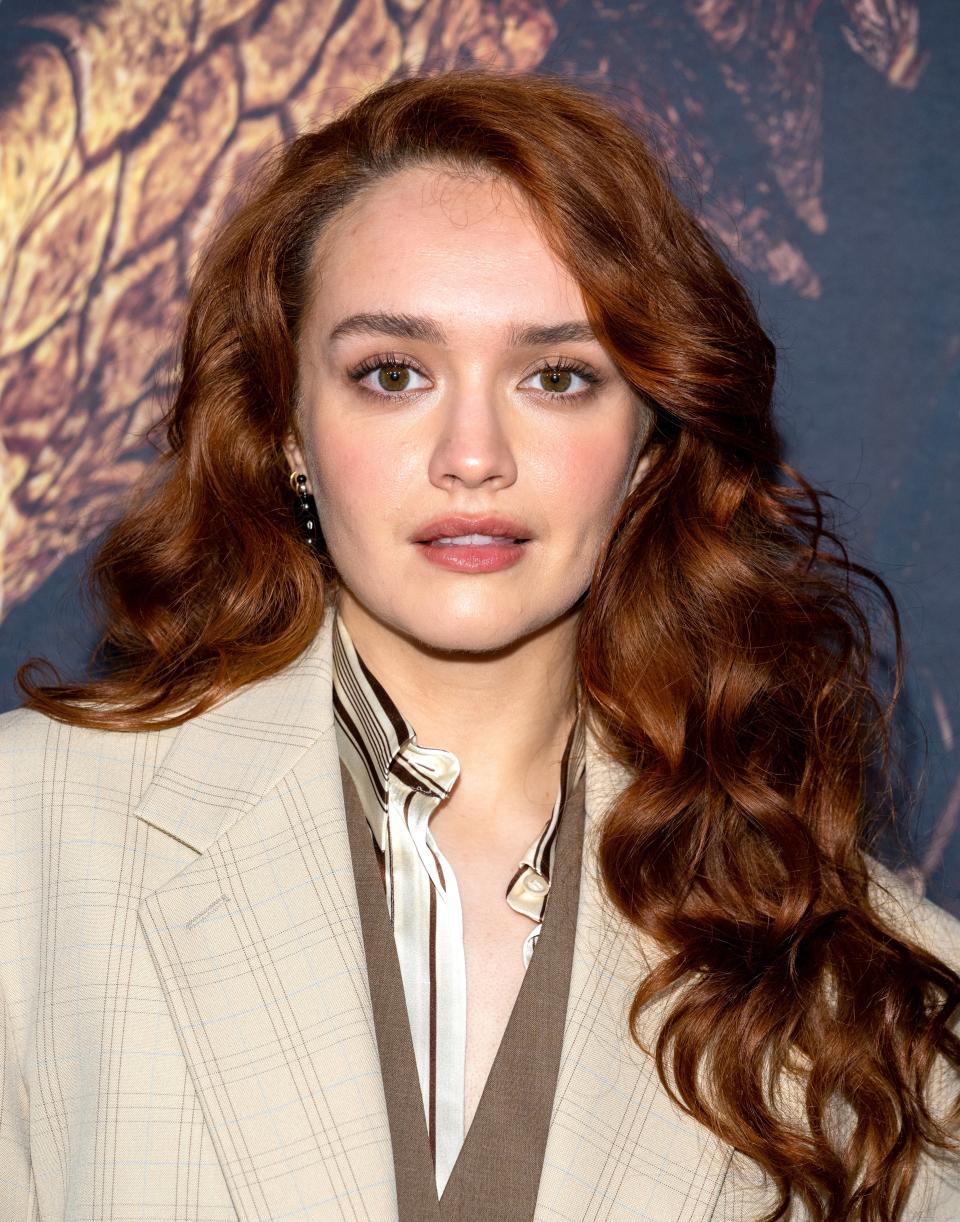 Olivia Cooke at a formal event, wearing a beige checked blazer over a striped shirt and brown vest, with long wavy hair