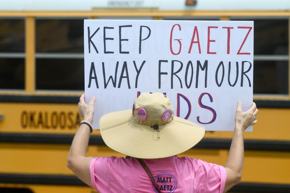 A member of the group Women Against Matt Gaetz holds a sign protesting the congressman as an Okaloosa County School bus passes. About two dozen members of the group gathered at the Okaloosa County School Board Administration building in Niceville Tuesday to oppose Gaetz's meeting with students at Niceville High School.