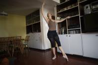 Carolina Wolf, who dances with Venezuela's national ballet, trains in her living room where she adapted her bookshelf to take the place of her ballet bar, during a lockdown to curb the spread of COVID-19 in Caracas, Venezuela, Tuesday, Aug. 11, 2020. The 42-year-old ballerina said her living room is four times smaller than the studio where she practiced daily at the famed Teresa Carreño Theater, and she doesn't dare do jumps in fear of injuring herself on the hard floor. (AP Photo/Ariana Cubillos)