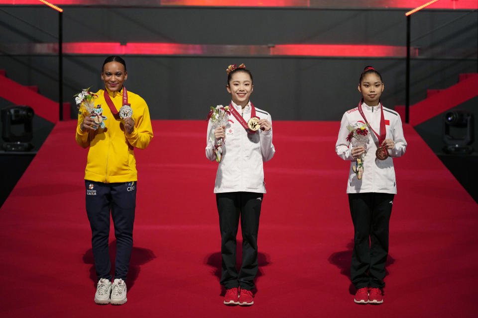 Wei Xiaoyuan, center, of China, with her gold medal, Rebeca Andrade, left, of Brazil, with her silver medal, and Luo Rui, of China, pose for photos and video during the victory ceremony for the women's uneven bars final in the FIG Artistic Gymnastics World Championships in Kitakyushu, western Japan, Saturday, Oct. 23, 2021. (AP Photo/Hiro Komae)
