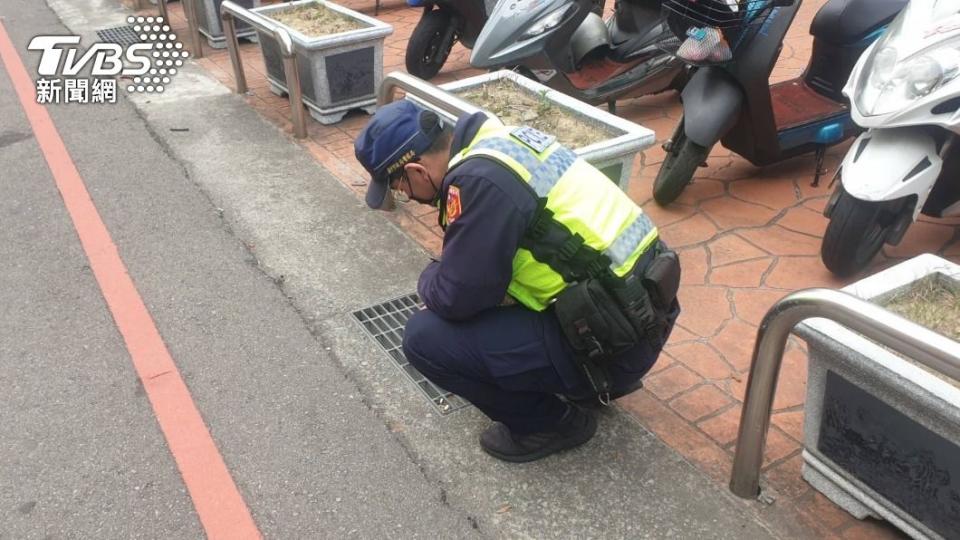 警方蹲在水溝蓋前，用自己長鍊鑰匙串，勾起婦人掉在水溝內的鑰匙。（圖／警方提供）