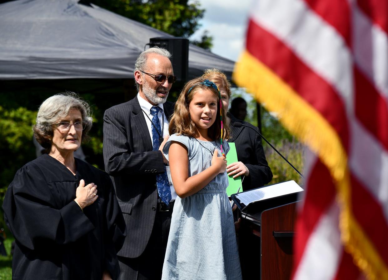 Lola Gomez, 9, of Woburn, whose mother, Sara, is becoming a new citizen, recites the Pledge of Allegiance with Magistrate Judge Katherine Robertson and Jospeh Forte of U.S. Citizenship and Immigration Services.