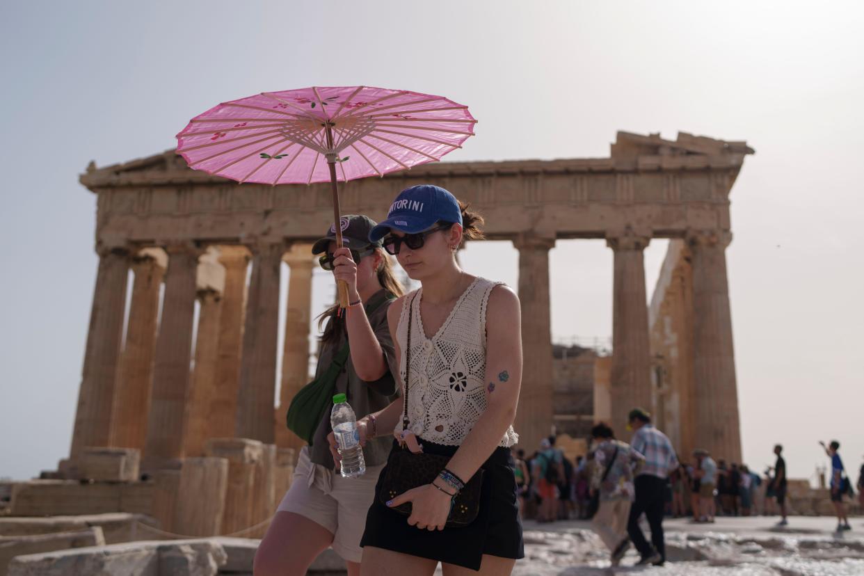 Tourists with an umbrella walk at the Parthenon at the ancient Acropolis in central Athens, which was closed for five hours during the day earlier this summer due to being too hot. (AP)