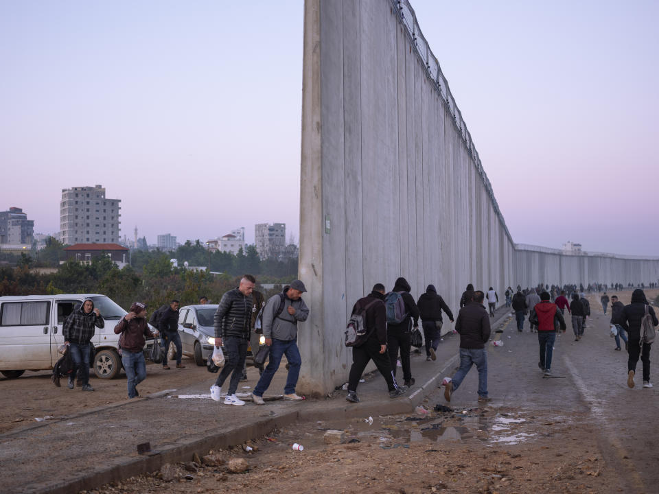 FILE - Palestinians cross into Israel from the West Bank through an opening in the Israeli separation barrier between the West Bank town of Qalqilya and the Israeli Kibbutz Eyal, Feb. 27, 2022. (AP Photo/Oded Balilty, File)