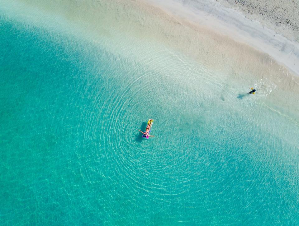 overhead view of two people in turquoise water along a white sand beach