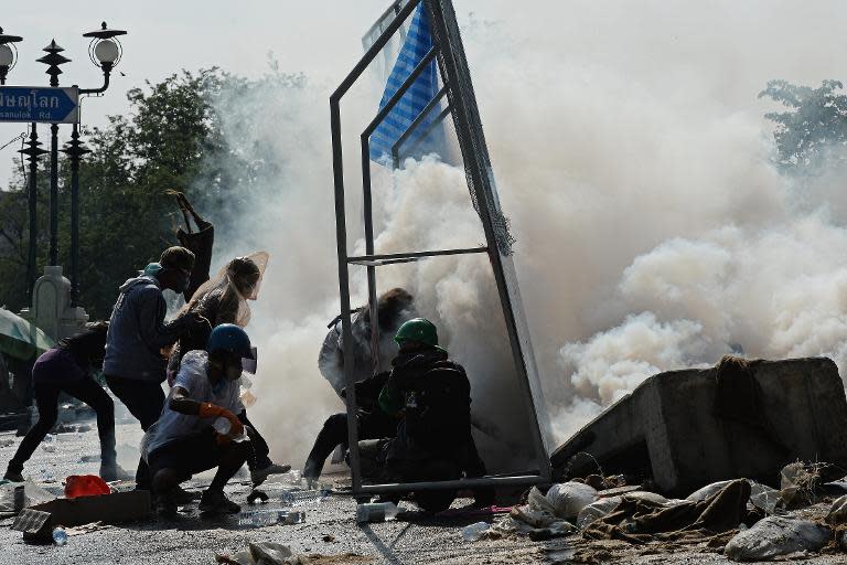 Thai anti-government protesters shield themselves behind a fence as they clash with the police during an ongoing rally outside Government House in Bangkok on December 2, 2013