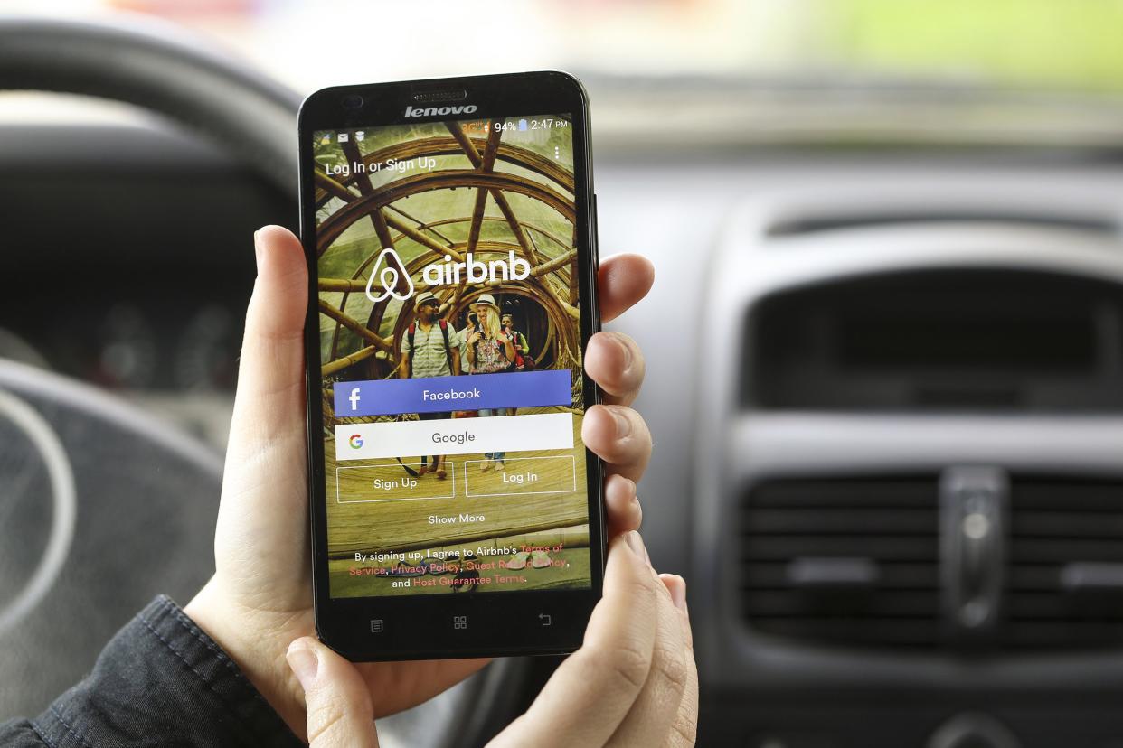 Woman's hands holding a smartphone with Airbnb app opened while sitting in the driver's seat in a car, selective focus, blurred background