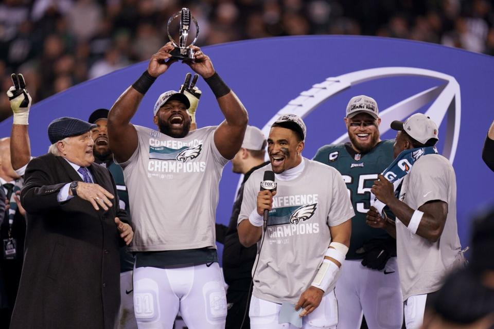 Philadelphia defensive tackle Fletcher Cox hoists the George Halas Trophy next to Jalen Hurts and Terry Bradshaw.