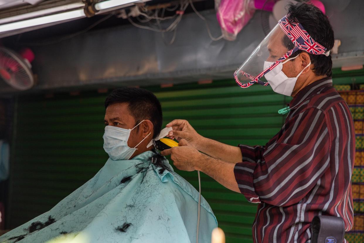 A Thai barber gives a man a haircut while wearing a face mask and shield after Thailand's lockdown was partially lifted on May 3, 2020, in Bangkok.