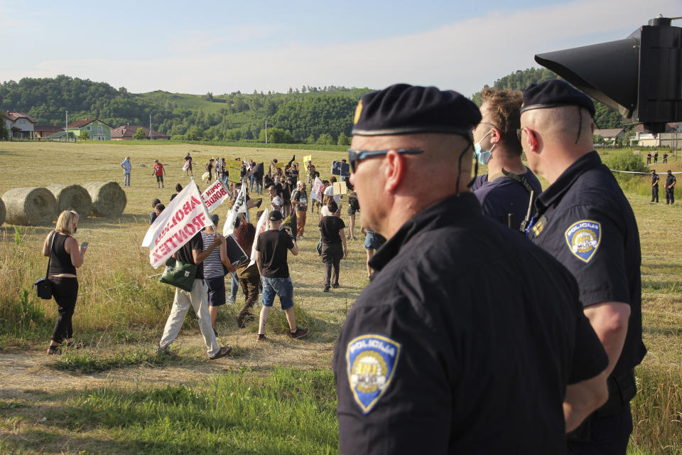 FILE - Croatian police officers stand as people walk with banners during a protest against the violent pushbacks of migrants, allegedly conducted by Croatian police, near the border crossing between Croatia and Bosnia Herzegovina in Maljevac, Croatia, on June 19, 2021. An independent investigative group on Thursday April 6, 2023 accused Croatian officials and police of using a clandestine WhatsApp group to share sensitive information about migrants trying to enter the country. (AP Photo/Edo Zulic, File)