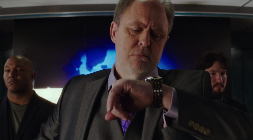 A close up of John Lithgow as he looks down on the watch on his wrist