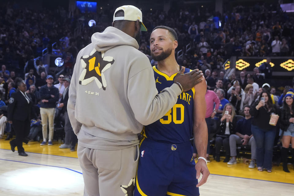 Injured Los Angeles Lakers forward LeBron James, left, talks to Golden State Warriors guard Stephen Curry during halftime of an NBA basketball game in San Francisco, Thursday, Feb. 22, 2024. (AP Photo/Jeff Chiu)