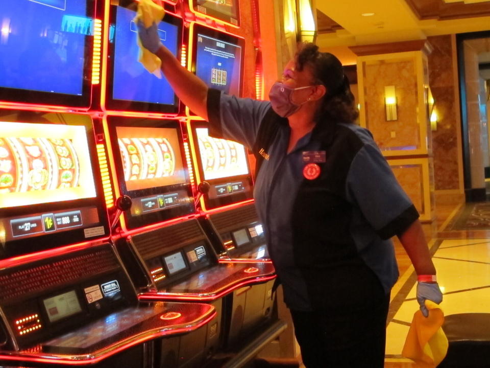 Jeorganna Barnes, a worker at Harrah's casino in Atlantic City, N.J., wipes slot machines with disinfectant Wednesday, July 1, 2020, as the casino prepared to reopen after 3 1/2 months of being shut down due to the coronavirus. Five of Atlantic City's casinos will reopen on Thursday, while three others, including Harrah's, will open Friday. (AP Photo/Wayne Parry)