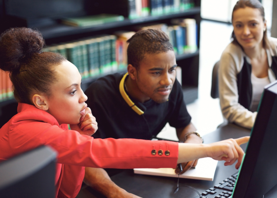 A group of college students working together on a group project in a library.