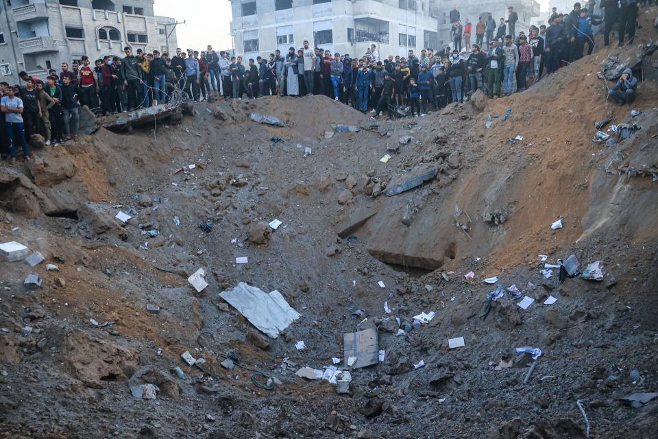 Palestinians stand on the edge of a crater after an Israeli strike in Rafah in the southern Gaza Strip on December 3, 2023.