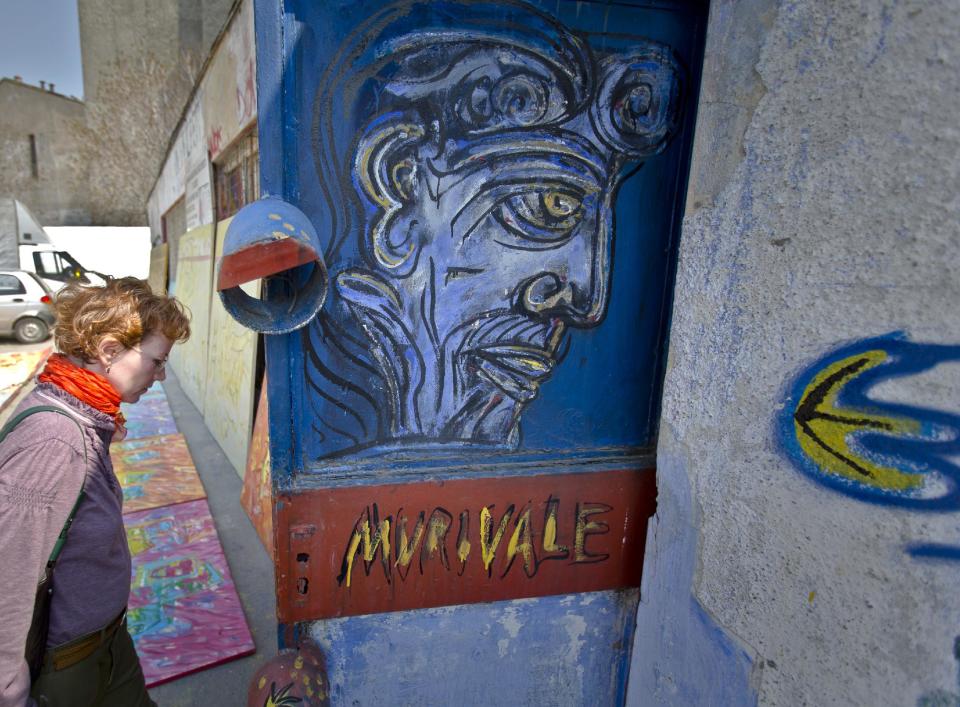 In this photo taken on April 4, 2013, a woman enters a storage room containing works by Romanian artist Vasile Muresan, known as Murivale, in a parking lot, in Bucharest, Romania. The white-bearded painter can often be seen sitting on his colorful canvasses which he displays in the street followed by the street dogs which are his companions and also inspire his work. The 56-year-old, whose home city is Bistrita_the Transylvanian town associated with the legendary Count Dracula_ has been painting with passion since he was a teen, producing vivid works of Monaco, the streets of Paris, the hurly burly of the Romanian capital and huge colorful more abstract canvasses. (AP Photo/Vadim Ghirda)