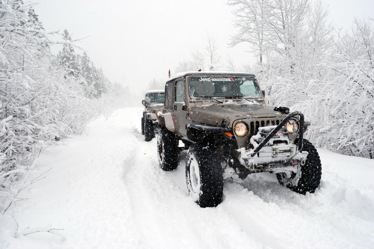 Two light brown Jeeps driving through deep snow.