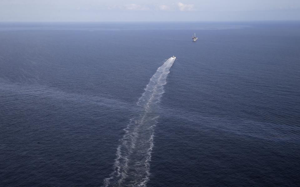 FILE- In this March 31, 2015 aerial photo, the wake of a supply vessel heading towards a working platform crosses over an oil sheen drifting from the site of the former Taylor Energy oil rig in the Gulf of Mexico, off the coast of Louisiana. A new federally led estimate of oil seeping from a platform toppled off Louisiana 14½ years ago is below other recent estimates. But the report contradicts the well owner’s assertions about the amount and source of oil. Oil and gas have been leaking into the Gulf of Mexico since a subsea mudslide caused by Hurricane Ivan on Sept. 15, 2004 knocked over a Taylor Energy Co. production platform. (AP Photo/Gerald Herbert, File)