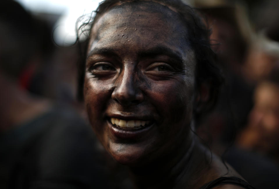 In this photo taken on Friday, Sept. 6, 2019, a woman painted with black grease smiles as she takes part at the traditional festivities of the Cascamorras festival in Baza, Spain. During the Cascamorras Festival, and according to an ancient tradition, participants throw black paint over each other for several hours every September 6 in the small town of Baza, in the southern province of Granada. The "Cascamorras" represents a thief who attempted to steal a religious image from a local church. People try to stop him, chasing him and throwing black paint as they run through the streets. (AP Photo/Manu Fernandez)