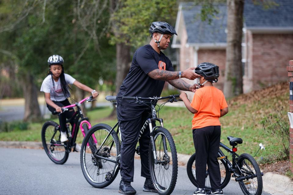 Tallahassee Police Department Sgt. Damon Miller adjusts the strap on his son's helmet while riding bikes with his two children through their neighborhood Thursday, March 17, 2022.