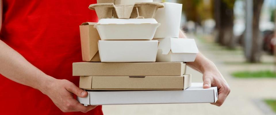 Diverse of paper containers for takeaway food. Delivery man is carrying pizza, Chinese noodles, burgers and coffee.