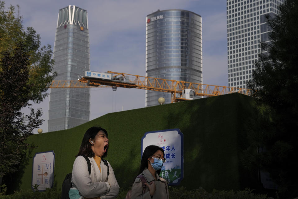 A woman holding a face mask yawns while passing by a construction crane at the Central Business District in Beijing, Monday, Oct. 18, 2021. China's economic growth sank in the latest quarter as a slowdown in construction and curbs on energy use weighed on its recovery from the coronavirus pandemic. (AP Photo/Andy Wong)