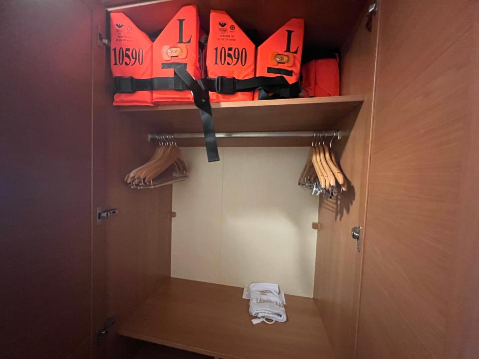 A closet with shelves, hangers, and orange life vests. 
