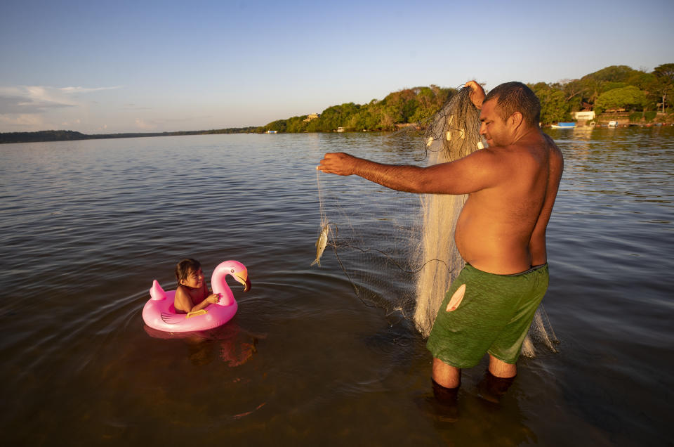 A fisherman plays with his daughter as he works in Alter do Chao, district of Santarem, Para state, Brazil, Wednesday, Aug. 26, 2020. This once pristine place is discovering that the perils of becoming a can’t-miss destination extend beyond hordes of weekend warriors sapping the unspoiled place of its charm. (AP Photo/Andre Penner)