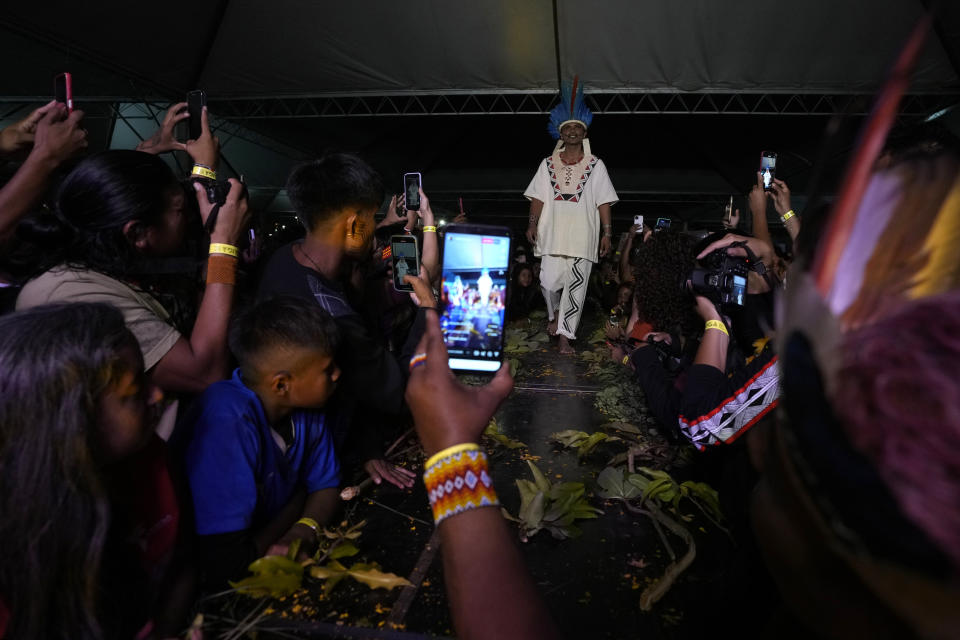 Attendees record as Indigenous models wear creations from Indigenous designers during a fashion event, as part of the Third March of Indigenous Women, to claim women's rights and the demarcation of Indigenous lands, in Brasilia, Brazil, Tuesday, Sept. 12, 2023. (AP Photo/Eraldo Peres)