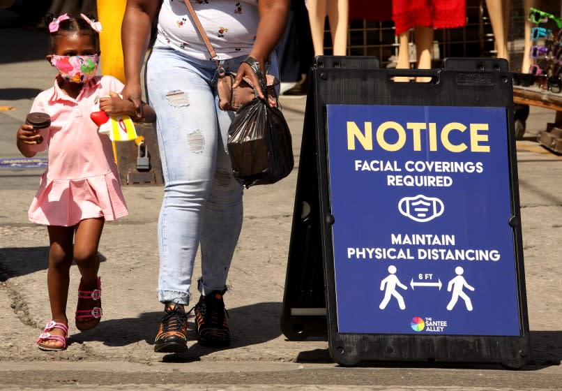 LOS ANGELES, CA - JUNE 30, A young shopper, wearing a mask to protect herself from coronavirus, shops with her mother on Santee Alley in the Garment District in downtown Los Angeles on June 30, 2020. Masks are required for shopping on Santee Alley and social distancing is advised, but hard to enforce. The shopping area has been open again for the past three weeks. (Genaro Molina / Los Angeles Times)