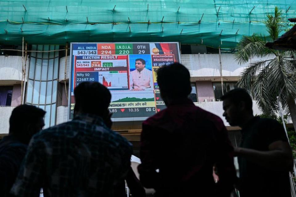 Pedestrians watch share prices on a digital broadcast outside the Bombay Stock Exchange (BSE) on the day of India's general election result in Mumbai on June 4, 2024