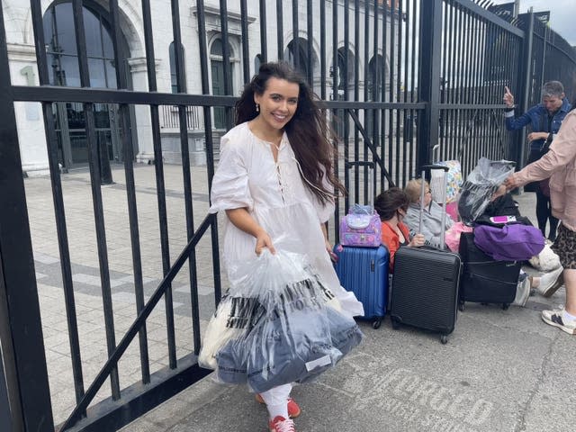 A woman stands in front of iron railings with carrier bags of merchandiseTour