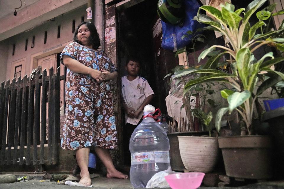 Devi Putri Eka Sari, una madre y ama de casa, en el exterior de su vivienda junto a su hijo, Satria Fareji, junto a las botellas que utiliza para recolectar agua, en Yakarta, Indonesia, el 13 de marzo de 2024. Sari, como millones de indonesios más en todo el país, compra agua en grandes recipientes rellenables o en botellas de plástico de un solo uso. (AP Foto/Dita Alangkara)