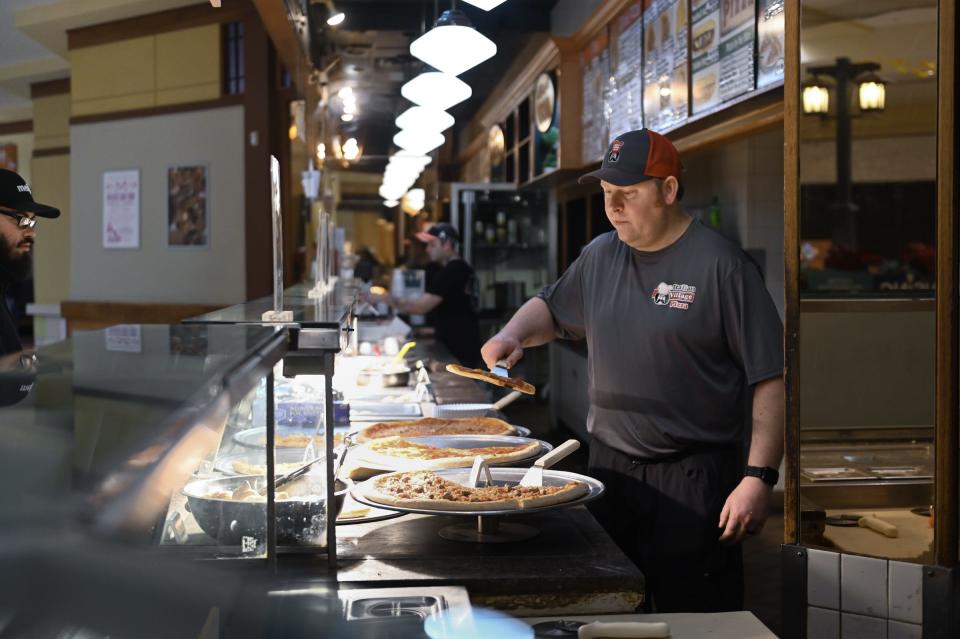Italian Village Pizza owner Ryan Marquardt prepares to put a slice of pizza in the oven Thursday, Feb. 1, 2024, at his pizza shop in the Lansing Mall.