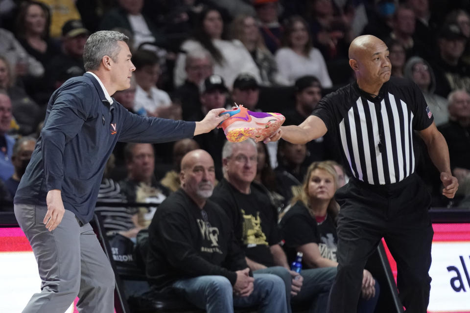An official give Virginia head coach Tony Bennett, left, one his players' shoes during the first half of an NCAA college basketball game against Wake Forest in Winston-Salem, N.C., Saturday, Jan. 21, 2023. (AP Photo/Chuck Burton)