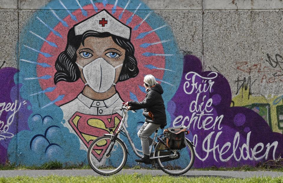 A woman on a bicycle passes a coronavirus graffiti by street artist 'Uzey' showing a nurse as Superwoman, the lettering reads "for the real heroes" on a wall in Hamm, Germany, on Easter Monday, April 13, 2020. (AP Photo/Martin Meissner)