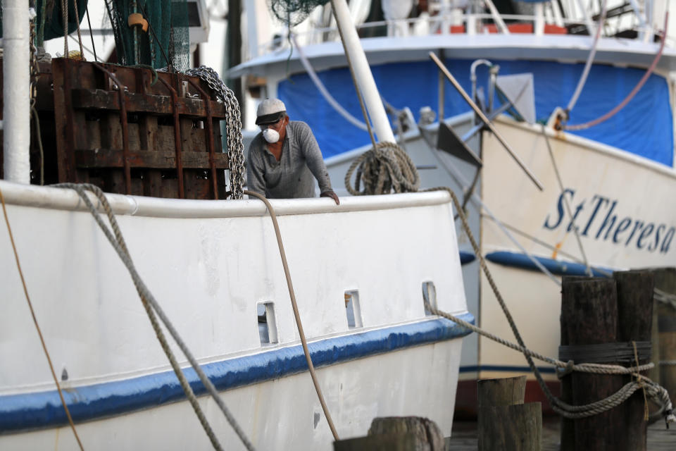 Minh Nguyen, wearing a mask out of fear of the catching the coronavirus, cleans his shrimp boat in Morgan City, La. Monday, May 11, 2020. He said he will not be going out for the start of the shrimping season due to low shrimp prices and fear of the virus. Attempts to curb the spread of COVID-19 have visited a kind of triple economic whammy on the state. As oil prices have plummeted, the industry laid off workers. Tourism has dried up, meaning more lost jobs. And one major tourist draw — cuisine built around fin fish, shrimp, oyster and crabs — is also suffering. (AP Photo/Gerald Herbert)