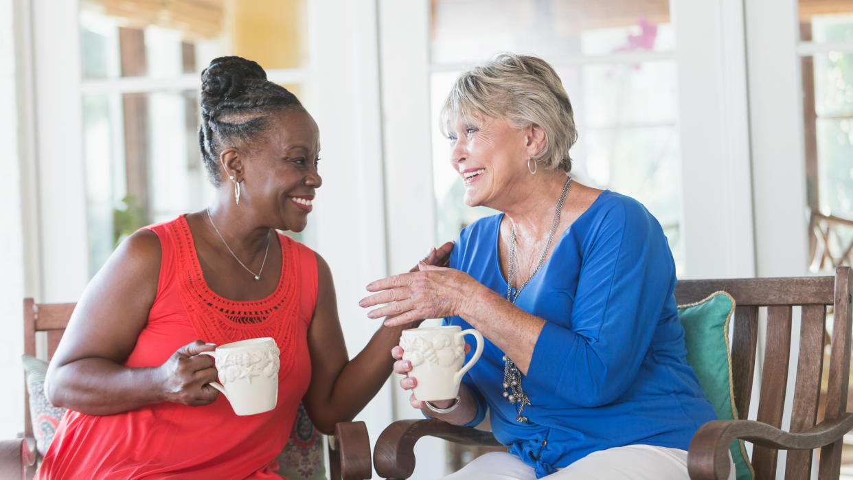 Two senior friends enjoying a talk on the outdoor porch while enjoying coffee