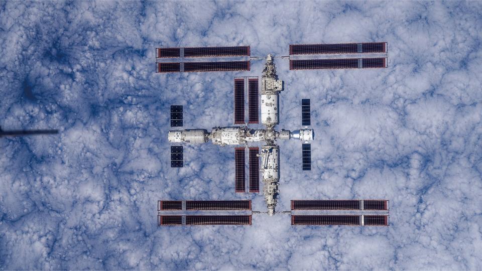 a large T-shaped space station is seen from above with the Earth below