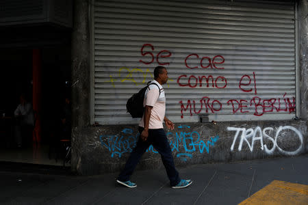 A man walks past a mural that reads, "It's falling like the Berlin Wall" during a blackout in Caracas, Venezuela March 27, 2019. REUTERS/Carlos Garcia Rawlins