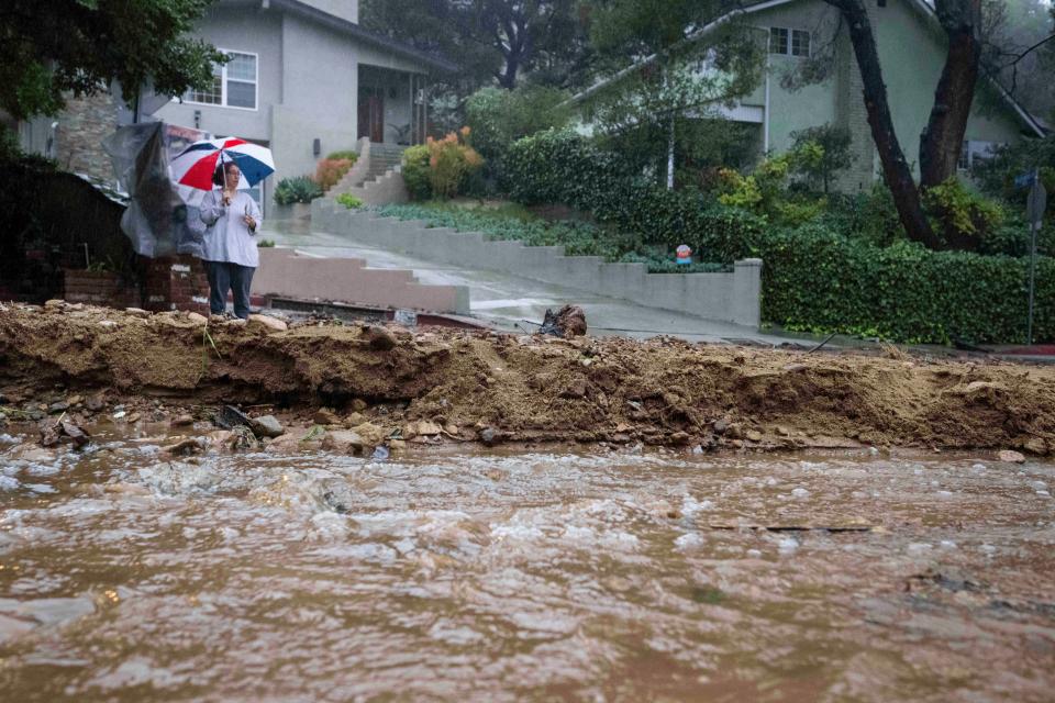 A resident keeps watch on Fredonia Drive in Studio City, Calif., where a mudslide is blocking the road during a rain on Tuesday, Jan. 10, 2023.