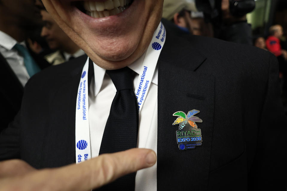 A members of the Saudi Arabia delegation points to his pin after the Bureau International des Expositions, or BIE, announced the vote Tuesday, Nov. 28, 2023 in Issy-les-Moulineaux, outside Paris. Saudi Arabia's capital Riyadh was chosen to host the 2030 World Expo, beating out South Korean port city Busan and Rome for an event expected to draw millions of visitors. Saudi Arabia's capital Riyadh was chosen on Tuesday to host the 2030 World Expo, beating out South Korean port city Busan and Rome for an event expected to draw millions of visitors. Riyadh was picked by a majority of 119 out of 165 votes by the member states. (AP Photo/Aurelien Morissard)