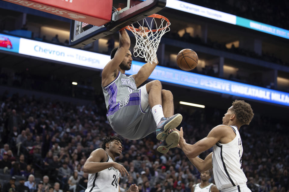 Sacramento Kings forward Trey Lyles (41) hangs from the rim after scoring a basket between Brooklyn Nets guard Cam Thomas (24) and forward Kessler Edwards (14) during the second half of an NBA basketball game in Sacramento, Calif., Tuesday, Nov. 15, 2022. The Kings won 153-121. (AP Photo/José Luis Villegas)