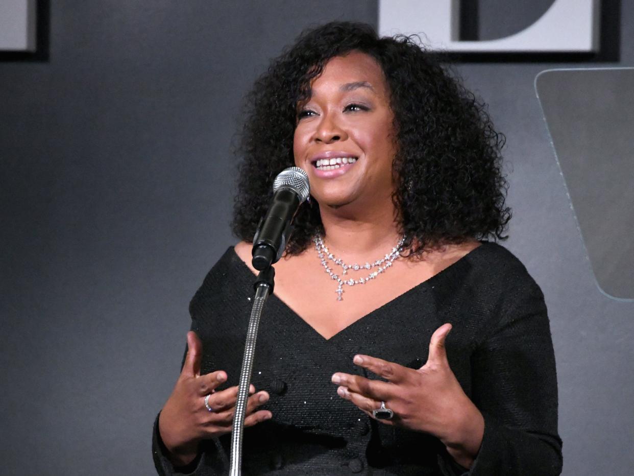 Shonda Rhimes wears black while speaking at a podium with a microphone