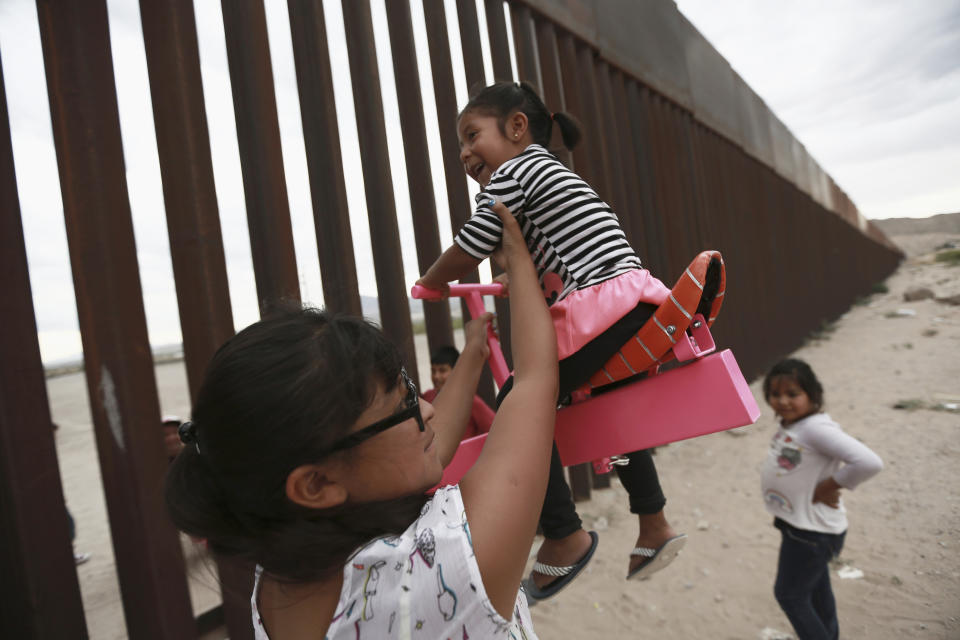 CORRECTS THE FIRST NAME OF THE PROFESSOR TO RONALD, NOT RONALDO AND THE LAST NAME OF THE PHOTOGRAPHER TO CHAVEZ, NOT TORRES - A woman with her little girls helps them play seesaw installed between the border fence that divides Mexico from the United States in Ciudad de Juarez, Mexico, Sunday, July 28, 2019. The seesaw was designed by Ronald Rael, a professor of architecture in California. (AP Photo/Christian Chavez)