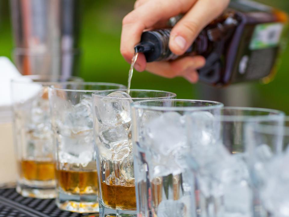 hand pouring liquor into glasses with ice at an outdoor bar for an event wedding