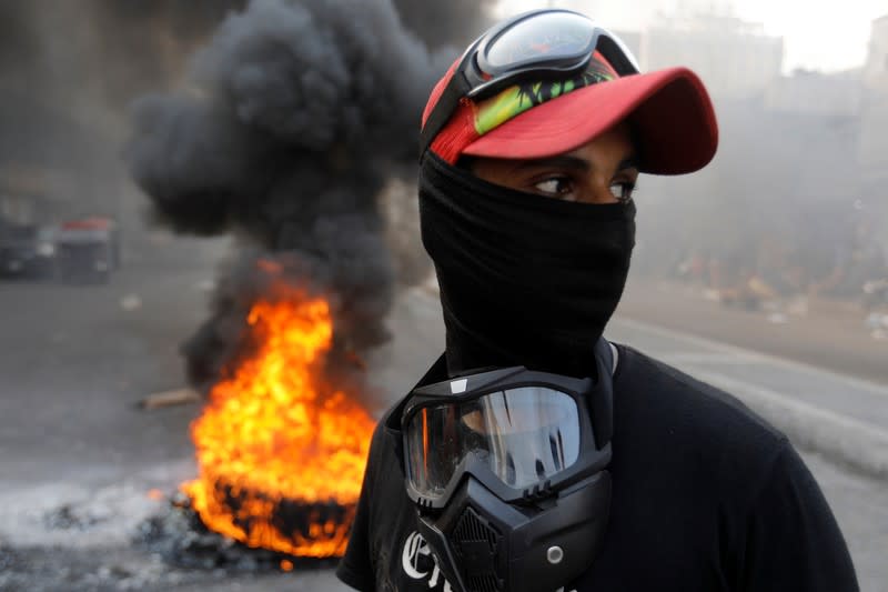 An Iraqi demonstrator is seen next to burning tires as he blocks the road during ongoing anti-government protests, in Baghdad