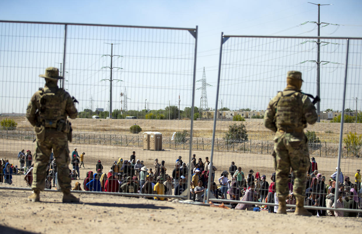 Migrants wait in line adjacent to the border fence under the watch of the Texas National Guard. (AP)